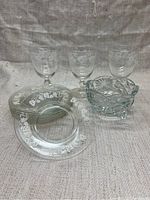 Overview of 6 etched glass plates, 6 etched glasses, and etched glass bowl against a cloth background