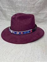 Side angled view showing shape, material, and decorative band on burgundy suede cowboy hat.