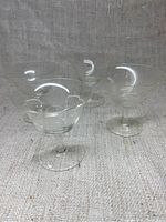 Four clear etched cocktail glasses shown together on textured cloth background, highlighting their shape and size.