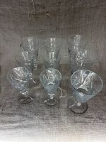 Overview of full set showing 9 clear crystal glasses with decorative patterning and varied heights.