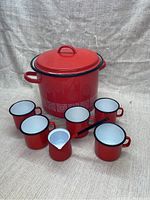 Red enamel pot with lid and six matching cups arranged around it, plus small creamer pot with handle and spout.