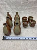 Photo showing 6 ceramic sake carafes and 4 sake cups next to a measuring tape indicating size around 3 inches wide for carafes.