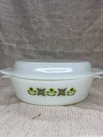 Front view of closed casserole dish showing floral design and handles on a cloth background.