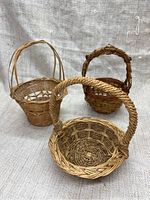 Front view of three mini woven baskets showing different weave styles and handles on a fabric background.