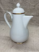 Full front view of the white porcelain pitcher showing shape, handle, and gold trim