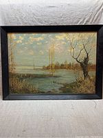 Full view of oil painting depicting a riverside landscape with trees and cloudy sky, framed in black wood