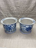 Front view of both porcelain plant pots showing blue floral patterns and matching saucers.