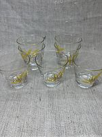 Front view of all seven vintage cocktail glasses arranged on fabric background showing yellow and black floral wheat motif.