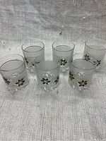 Top view of six vintage rocks glasses arranged in two rows on a textured beige fabric, showing the gold rim and floral designs.