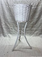 Full view of white wicker plant holder on three-legged metal stand, showing overall shape and height.