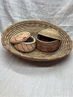 Large oval woven basket and two smaller round woven lidded baskets on fabric background.
