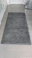 Rectangular grey shaggy area rug laid flat on floor, showing texture and size.