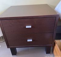 Front view of one brown bedside table showing two drawers with silver pulls and straight legs.