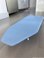 Small ironing board with blue cover placed flat on floor