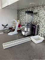 Breville blender with manual, Italian espresso cups with saucers, white storage bowls, and long white serving trays with gray pattern on kitchen counter