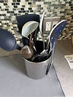 Various cooking utensils including serving spoons, tongs in a cylindrical stainless steel utensil holder.