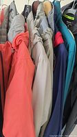 Seven various coats and jackets hung on a rack, showing diversity in style and color, emphasizing outerwear assortment
