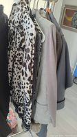 Photo showing four designer sweaters and jackets on hangers, including a leopard print jacket in front and several neutral toned pieces behind it.