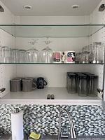Wide view of cabinet shelves holding coffee mugs, wine glasses, cognac glasses, and various drinking glasses including black tinted and clear glasses