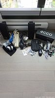 Photo showing Bose black wall mount speakers, headphones, power strip, cables, mouse, and accessories including Ecco shoe box