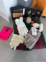Overall lot contents laid on plaid blanket including gloves, ear warmers, wine and cheese kit in black case.