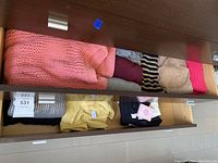 Top drawer with various folded medium and large sized ladies sweaters and shirts in peach, burgundy, cream, and striped patterns.