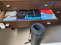 Drawer open showing neatly folded sport shirts and jackets in various colors including grey, black, blue, coral.