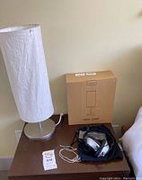 Two white cylindrical table lamps with fabric shades on a brown table next to a box for a yellow touch control lamp and an instructional manual or tag.