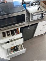 LG microwave and Black and Decker toaster oven displayed on counter with open drawers below showing flatware and kitchen tools