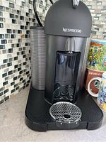Close-up front and side angle of black Nespresso coffee maker with water reservoir and pod holder