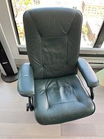 Full view of the green leather recliner chair with padded armrests and ergonomic backrest