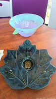 Multi-color art glass bowl and green leaf flower frog on wooden table.
