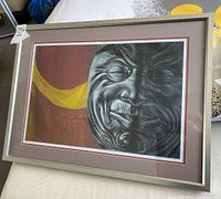 Framed limited edition signed original art print showing the detailed grayscale face and yellow abstract shapes on maroon background, with matte and silver frame.