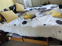 Photo of bed with bedspread and pillows, underneath are two wooden storage drawers on wheels containing linens and bedding.