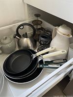 Drawer with non-stick frying pans, ceramic kettle, stainless steel kettle, two French presses, and a ceramic jar.