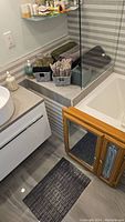 Photo showing the vanity doors with mirror and painted glass, towels in basket on tiled ledge, soap dispenser on countertop next to sink, and bath mat on tile floor.