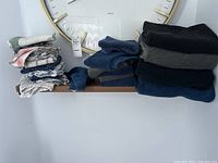 Folded bath towels, hand towels, facecloth, and kitchen towels stacked on a small wooden shelf under a large wall clock.