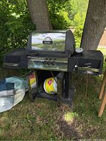 Front view of Broil Mate BBQ grill with black lid and side tables, propane tank stored below.