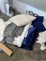 Photo showing stack of fleece blankets in grey, white, and blue colors along with throw pillows with different textures and colors.