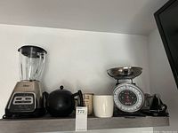 Full view of all items on shelf showing blender, teapot, mugs, kitchen scale, and apple peeler