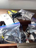 Wide view into drawer showing multiple plastic bags filled with cables, chargers, cords, and a Mastercraft power bar with batteries visible