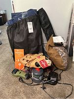 Photo showing inflatable mattress packed in black bag, tan Rawlings baseball glove, gray Woods fuel canister, and black electronic device on carpeted floor.