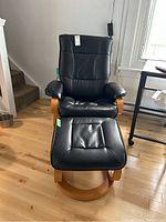 Front view of black vegan leather swivel lounge chair and matching ottoman on wooden bases.