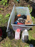 Photo of large clear plastic tote filled with various tools and accessories, with lid leaning against tote, and plastic containers of liquids and oil beside it.