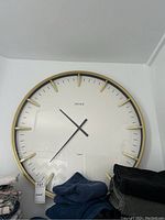 Full view of large round gold-toned frame clock mounted on the wall above folded clothes.