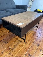 Side angle photo of a wood coffee table with metal legs and open shelves on each end, placed next to a gray sofa.