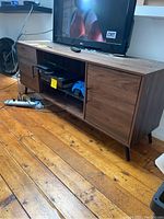 Full front view of wood credenza with TV on top, showing two side doors and middle open section with glass shelf and some electronics inside.