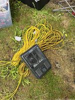 Black Thermosphere heater with one yellow extension cord underneath on grass