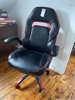 Front view of the black gaming chair with red stitching, showing seat, armrests, and base with wheels.