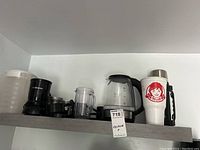Shelf with Salton glass electric kettle, La Reveuse personal blender parts, large Wendy's branded thermos, white plastic cup with lid, and plastic pitcher with lid.